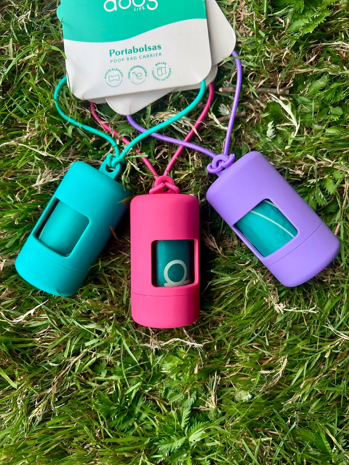 Turquoise, fuchsia and violet dog poop bag holders on grass with a box of biodegradable waste bags