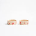 A pair of creamy beige handcrafted stoneware pet bowls with hand-painted red hearts.