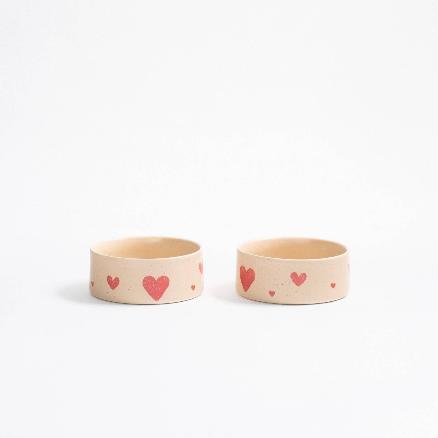 A pair of creamy beige handcrafted stoneware pet bowls with hand-painted red hearts.
