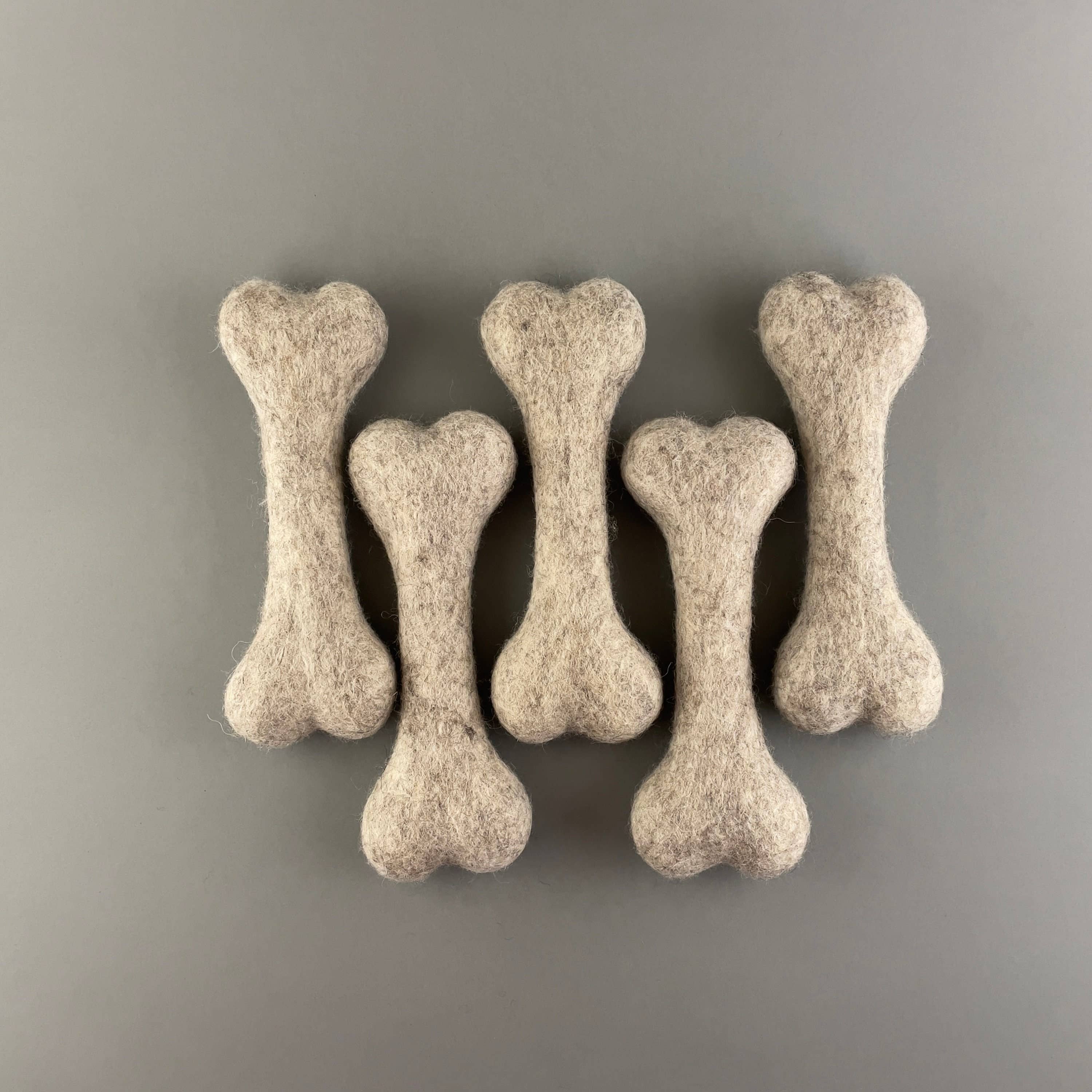 A handful of handmade 100% natural felted wool bone dog toy in an earthy light brown tone